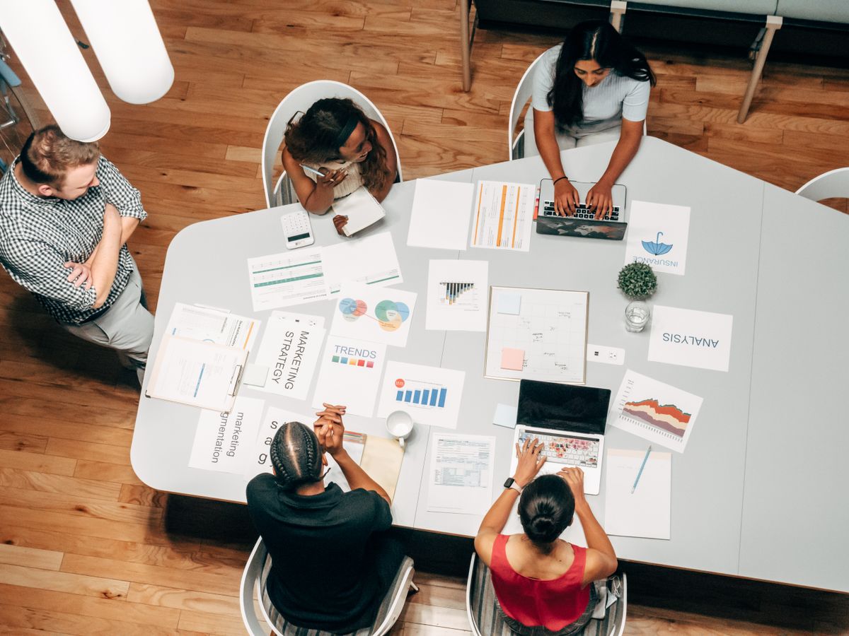 Cinq collaborateurs
    réunis autour d'une table de réunion couverte de tableaux et d'ordinateurs portables